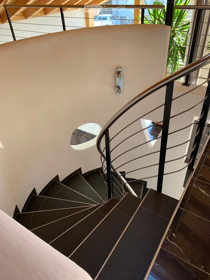 Spiral staircase with dark stone steps, modern metal railing, and a circular light fixture on the wall.
