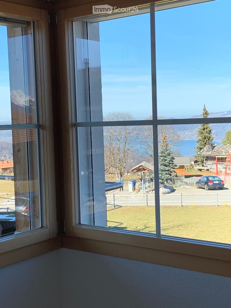 Empty room with large windows offering a scenic view of a lake, mountains, and surrounding landscape.