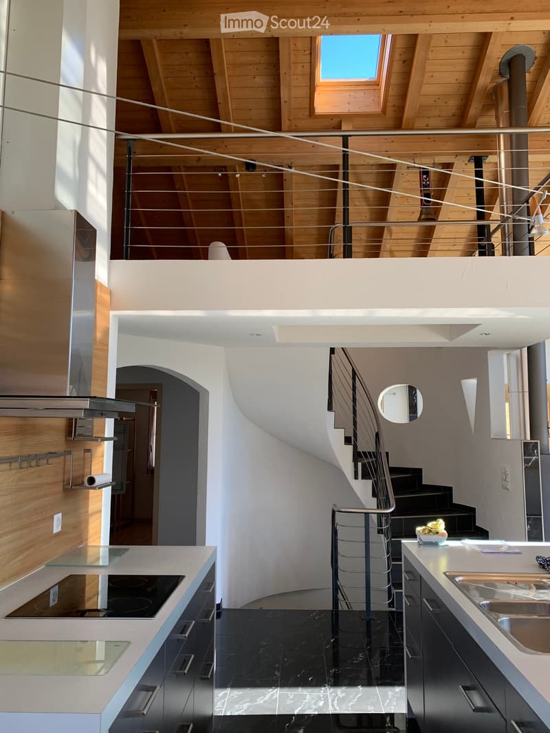 Modern kitchen with black marble flooring, white countertops, stainless steel appliances, and a sleek staircase leading to an upper level with wooden beams and skylights.