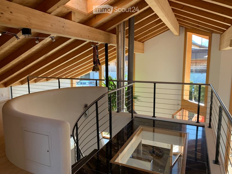 Spiral staircase with wooden beams, glass railing, and modern lighting fixtures.