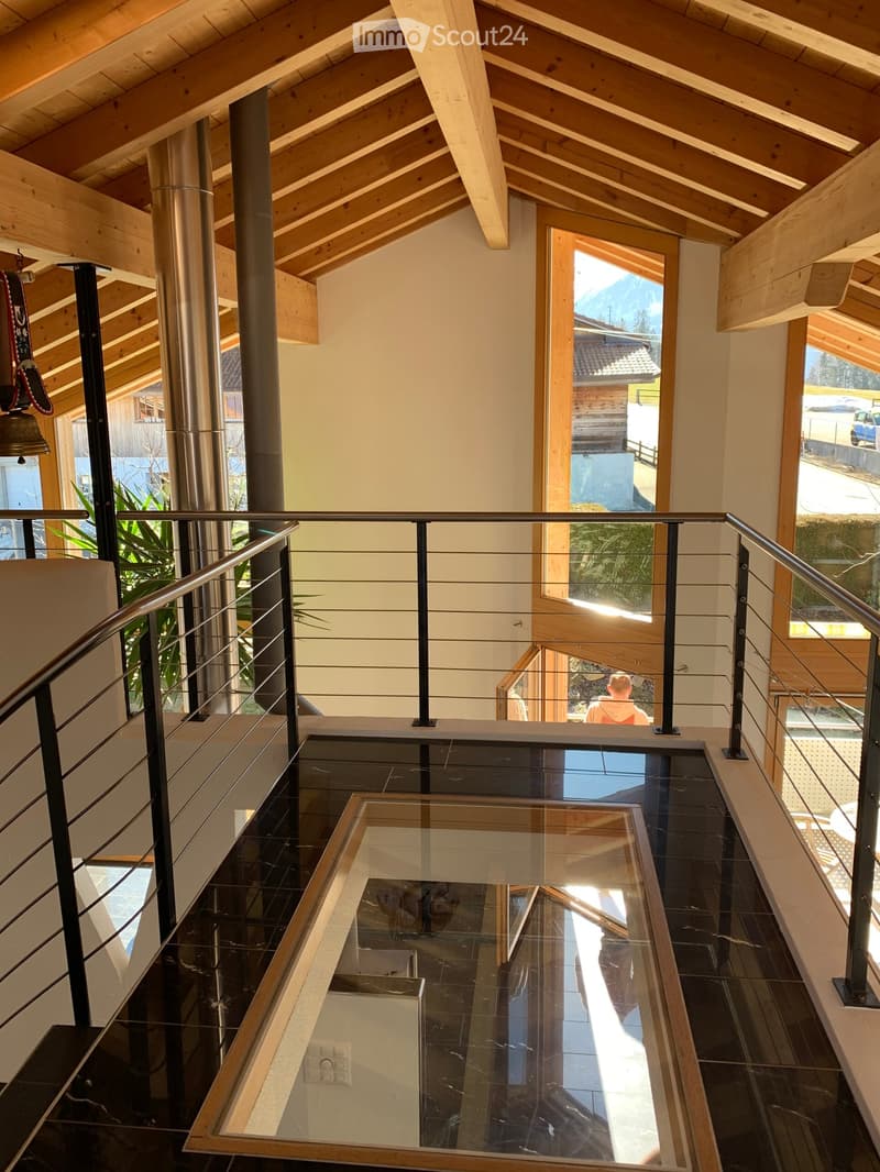 Modern hallway with wooden beams, glass floor, metal railing, and large windows offering a view of the outdoors.
