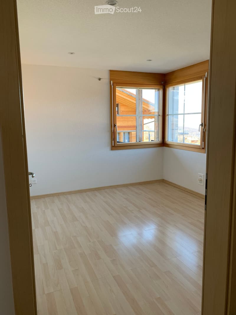 Empty room with light wooden flooring, white walls, and large windows with wooden frames, offering a view of a wooden structure outside.