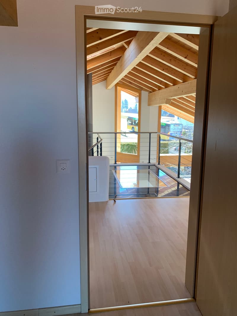 Modern hallway with wooden flooring, glass railing leading to a balcony area with wooden beams and outdoor view.