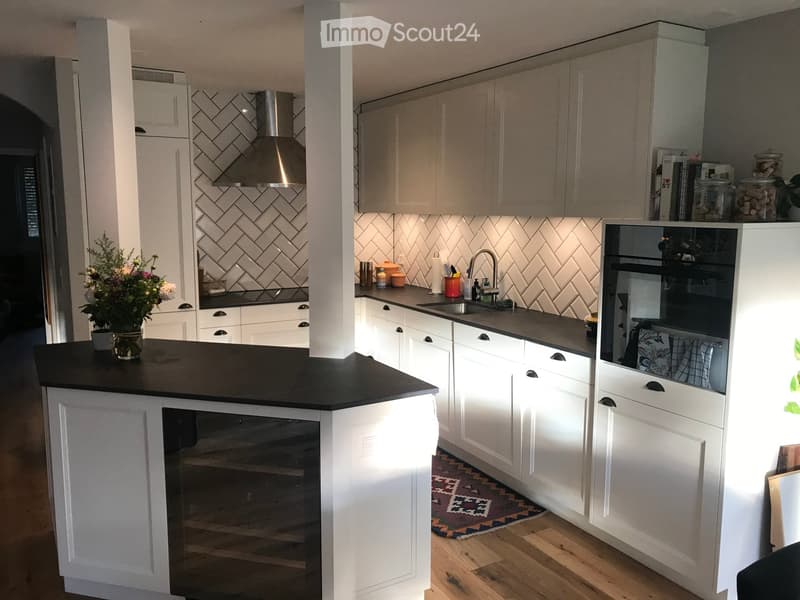 Modern kitchen with white cabinets, black countertops, stainless steel appliances, and a central island. Features a sink, faucet, and decorative vase on the counter.