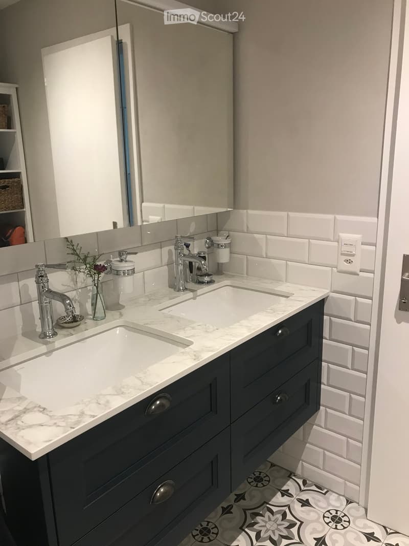 Modern bathroom with double sink vanity, marble countertop, dark blue cabinetry, and decorative tile flooring.