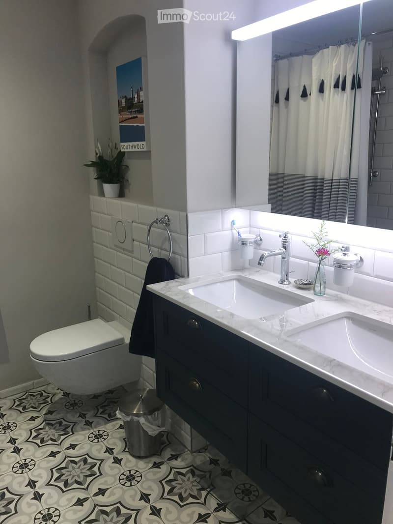 Modern bathroom with double sink, marble countertop, dark cabinets, patterned tile floor, and a shower area with a curtain.