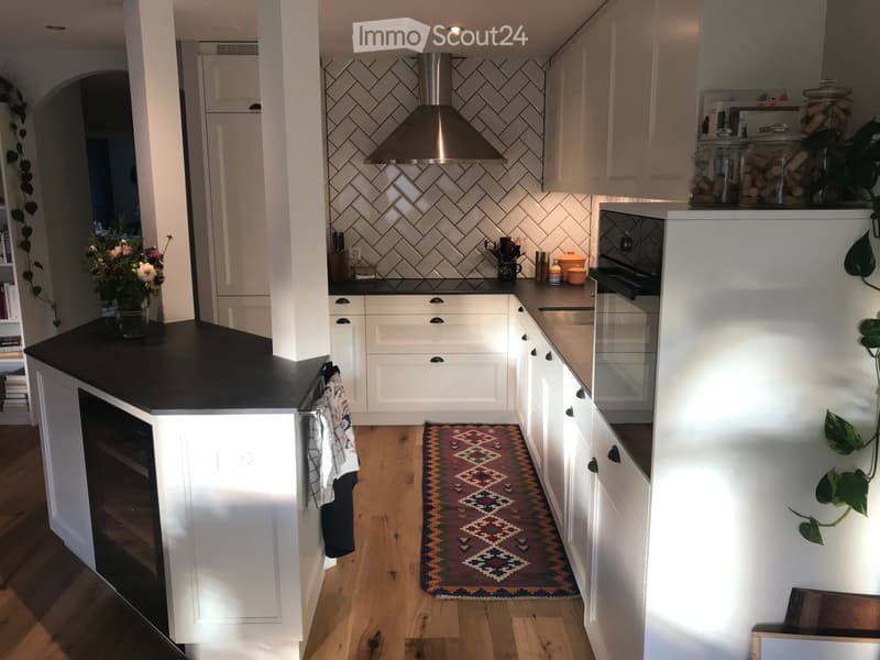 Modern kitchen with white cabinets, black countertop, stainless steel range hood, and a colorful patterned rug on the floor.