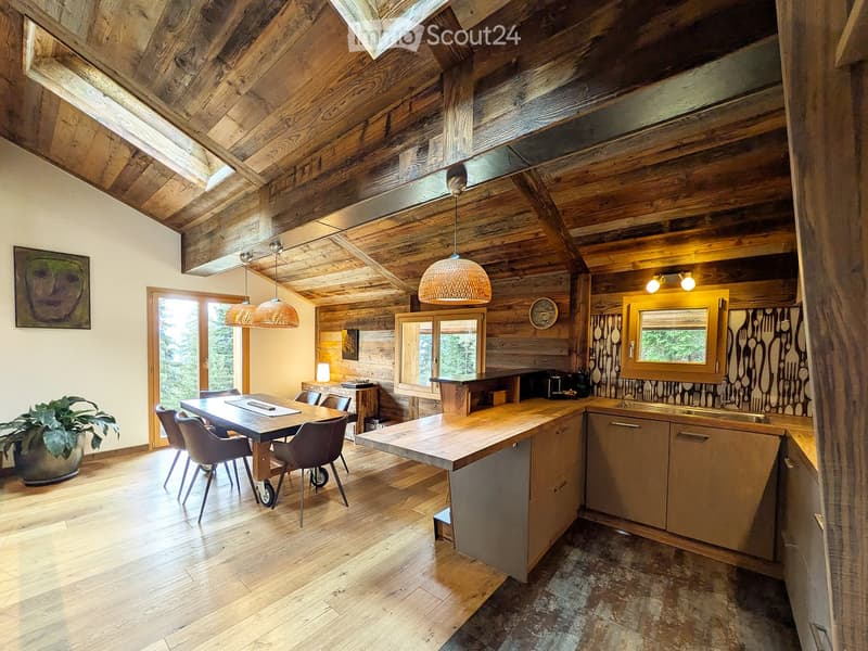 Modern kitchen with wooden beams, exposed wooden ceiling, pendant lights, island, dining table, chairs, and a sink area.