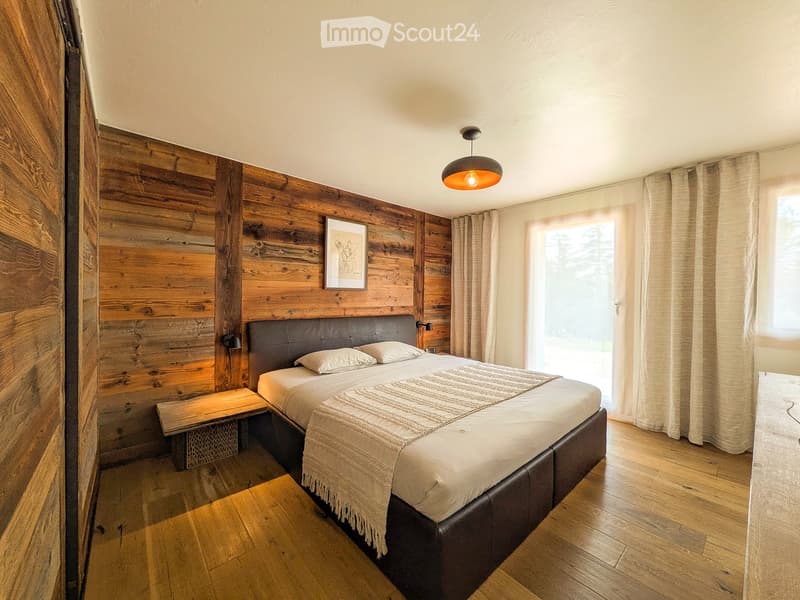 Cozy bedroom with wooden walls, a large bed with leather headboard, a bench at the foot of the bed, and a picture frame on the wall.