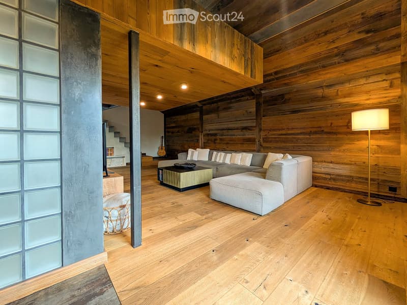 Modern living room with wooden walls and floors, a grey sectional sofa, coffee table, floor lamp, and a guitar in the background.