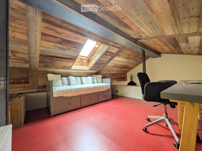 Cozy attic bedroom with wooden walls and ceiling, red carpet, sofa bed, desk, and chair.