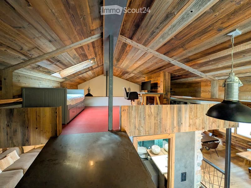 Loft-style room with exposed wooden beams, a sofa, a bed, a desk with a computer, and a small bathroom area.
