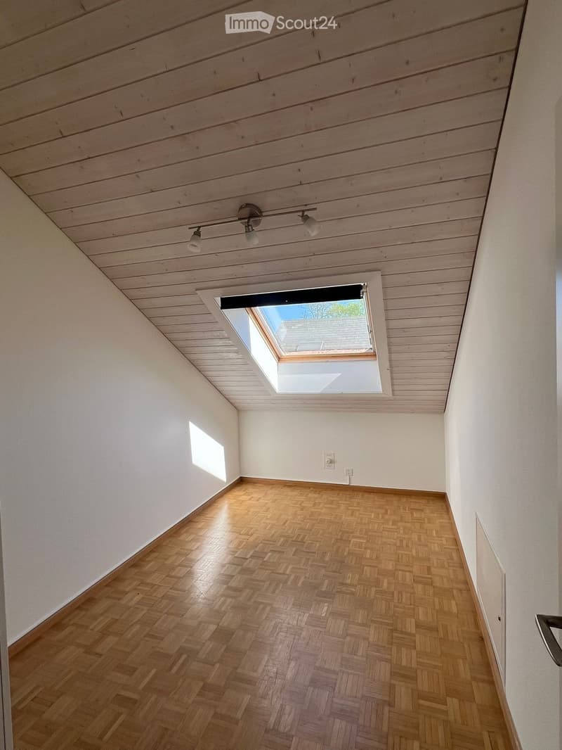 Empty room with wooden herringbone flooring, white walls, and a skylight window letting in natural light. The ceiling features wooden paneling and integrated lighting fixtures.