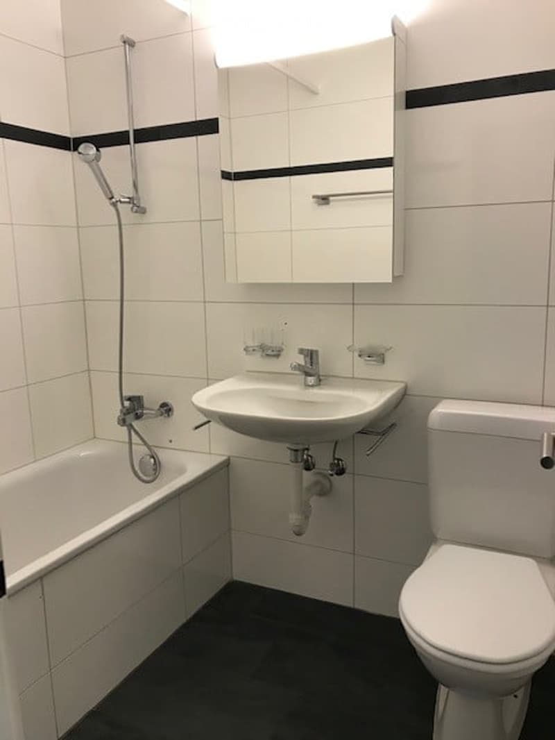 Modern bathroom with white tiles, black trim, bathtub, sink, toilet, and mirror.