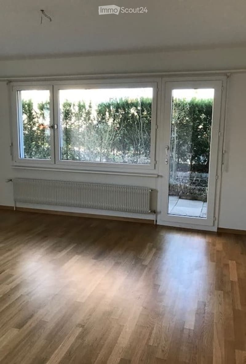 Empty room with wooden flooring, large windows, and a radiator. No furniture or equipment present.