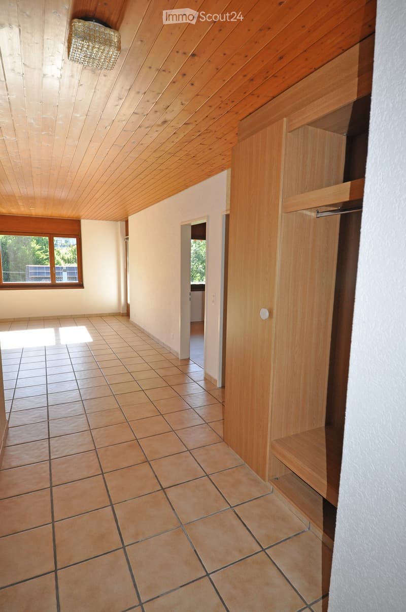 Empty hallway with tiled floor, wooden walls, and a window on one side. The ceiling has wooden beams and a chandelier fixture.