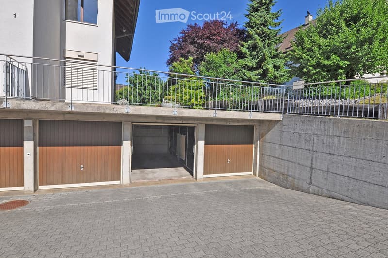 Multi-car garage with wooden doors, concrete walls, and a metal balcony railing above.
