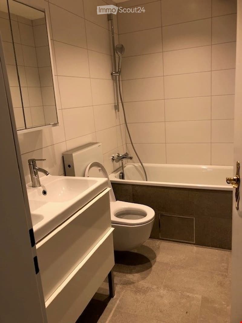 Modern bathroom with white tiles, a sink, toilet, bathtub, and a mirror above the sink.