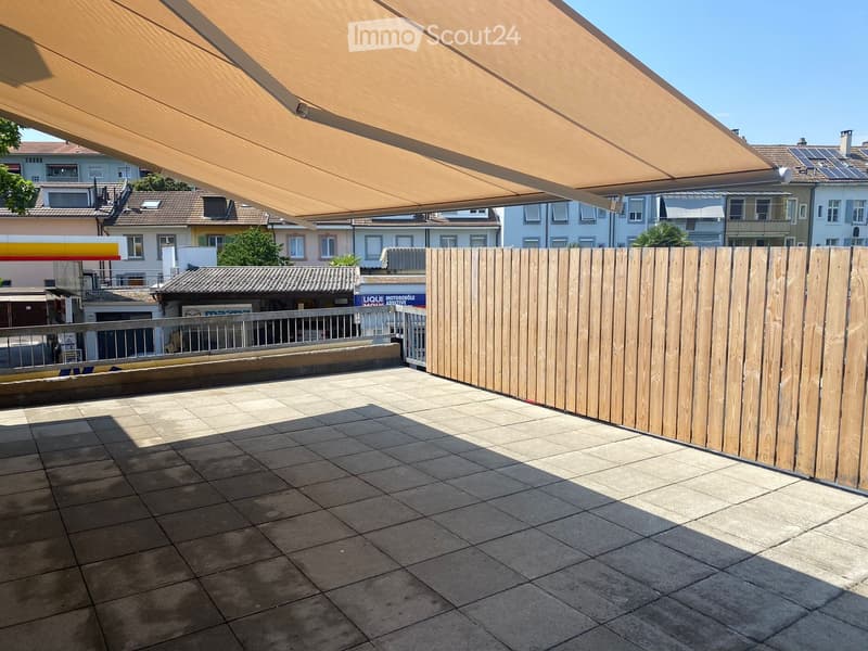 Balcony with tiled floor, wooden fence, and retractable awning, overlooking a residential area.