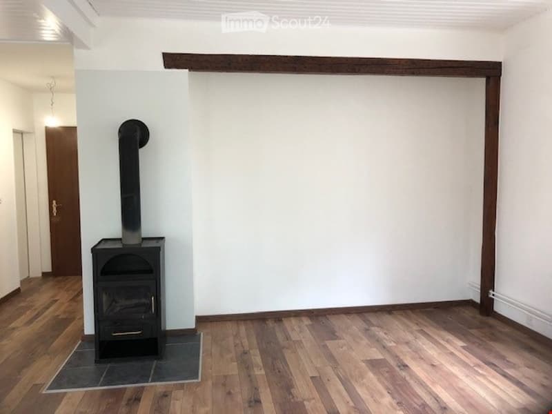 Empty room with wooden flooring, white walls, and a black fireplace with a chimney. No furniture or equipment present.