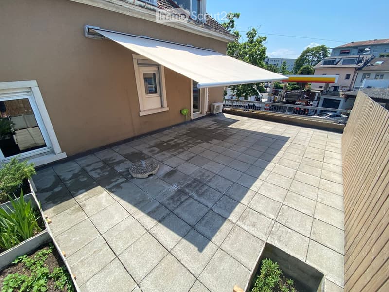 Balcony with tiled floor, retractable awning, small garden beds, and wooden fence.
