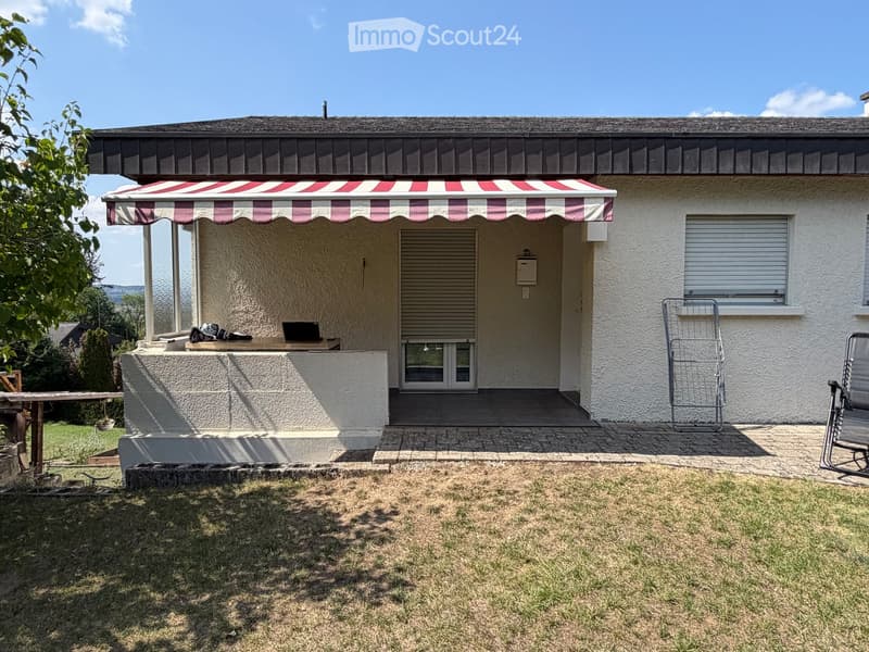 Single-story house with a covered patio area, outdoor furniture, and a grassy lawn.