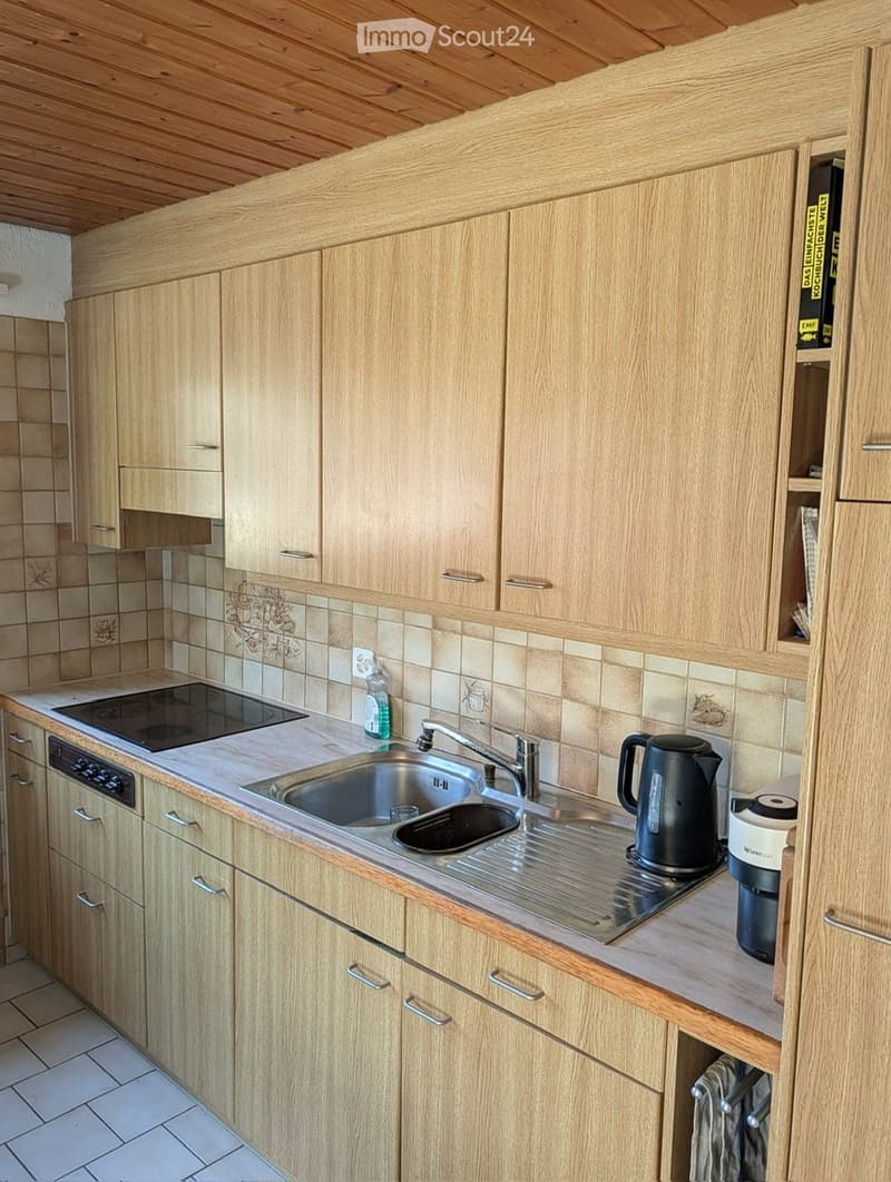 Modern kitchen with light wooden cabinets, stainless steel sink, electric stove, dishwasher, and countertop appliances including a coffee maker and kettle.