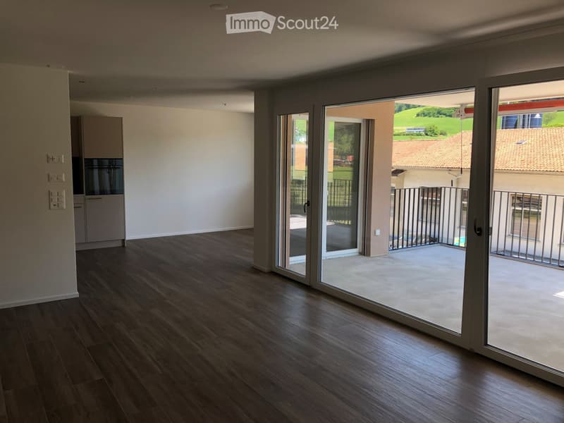 Empty room with wooden flooring, large sliding glass doors leading to a balcony, and white walls.