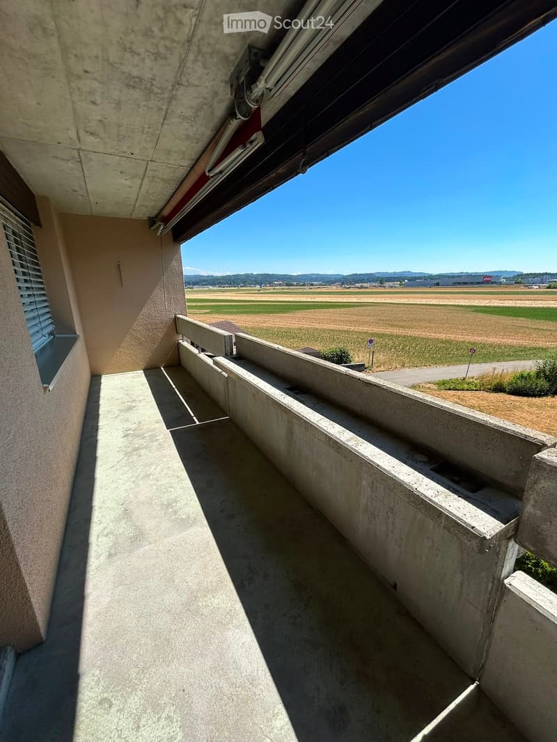 Concrete balcony with a view of open fields and distant mountains under a clear blue sky.