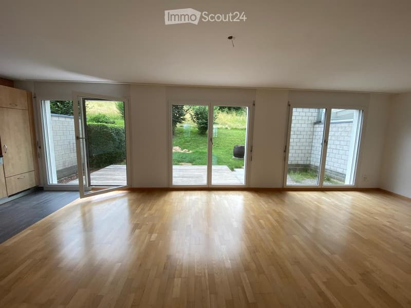 Empty room with wooden flooring, large sliding glass doors leading to a patio, and a view of a garden.