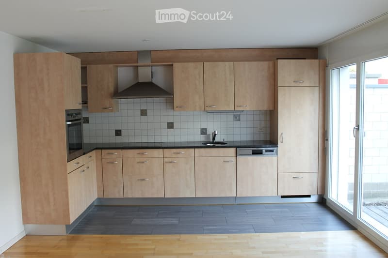 Modern kitchen with light wooden cabinets, stainless steel appliances, and a large window providing natural light.