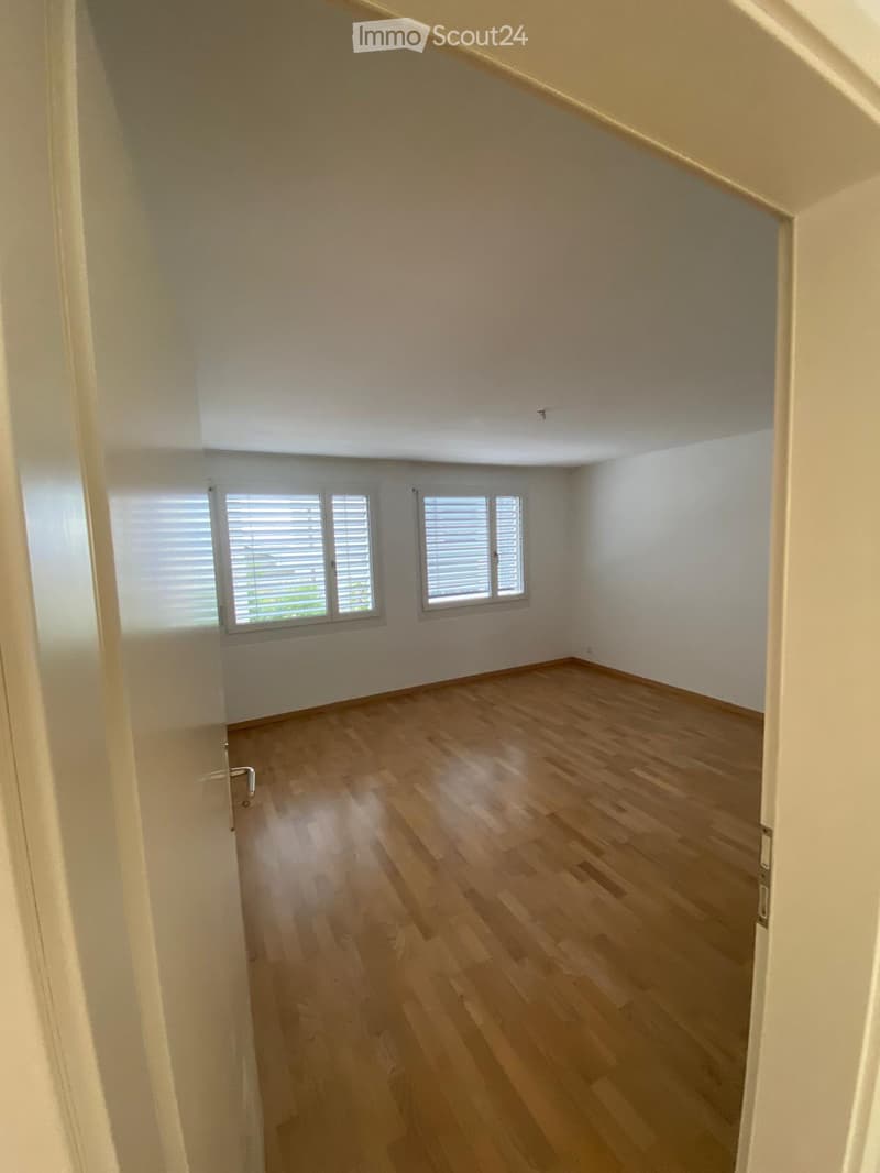 Empty room with wooden flooring, white walls, and two windows with blinds.