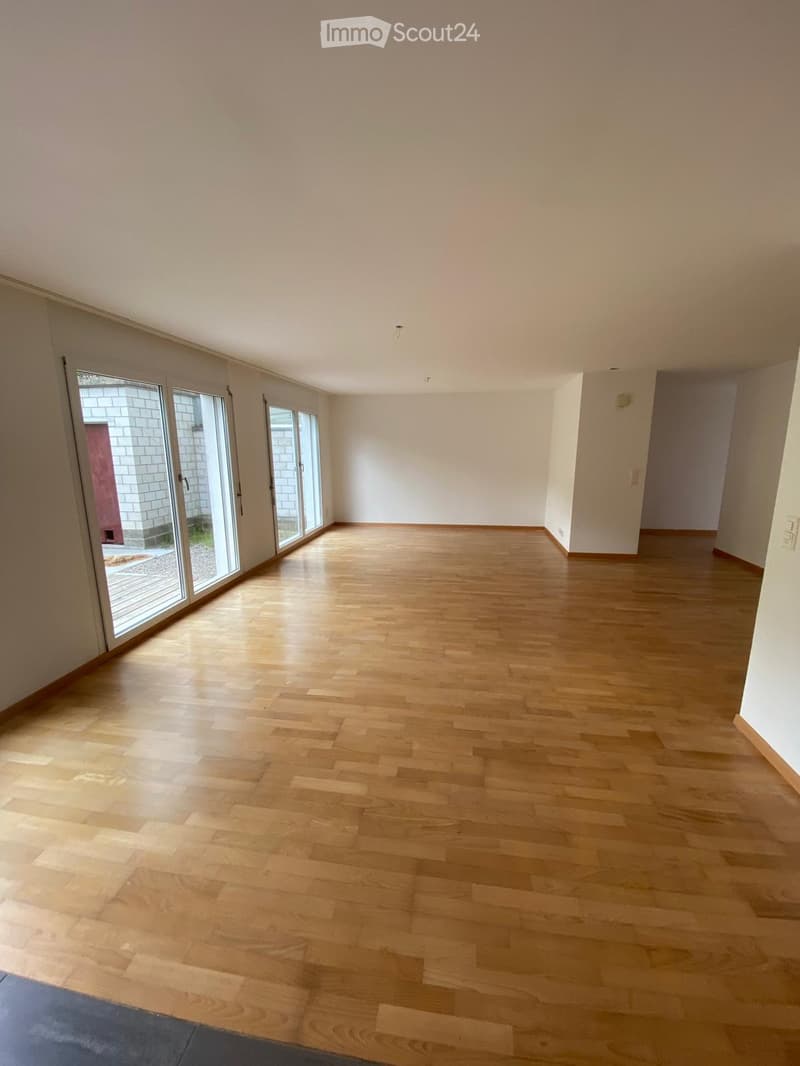 Empty room with light wooden flooring and white walls, featuring large glass sliding doors leading to an outdoor area.