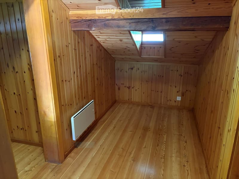 Empty wooden room with wooden walls, ceiling, and floor, featuring a small window and a radiator on one wall.