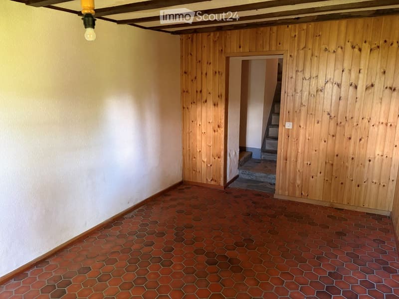 Empty hallway with wooden panel walls, red hexagonal tiled floor, and a visible staircase leading upwards.
