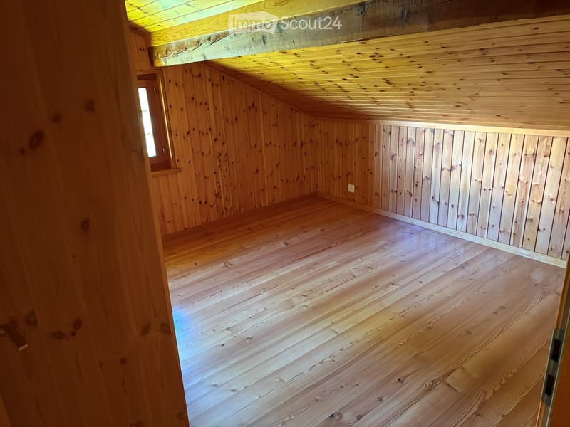 An empty wooden room with exposed wooden beams on the ceiling and walls, featuring a wooden floor and a small window on one side.
