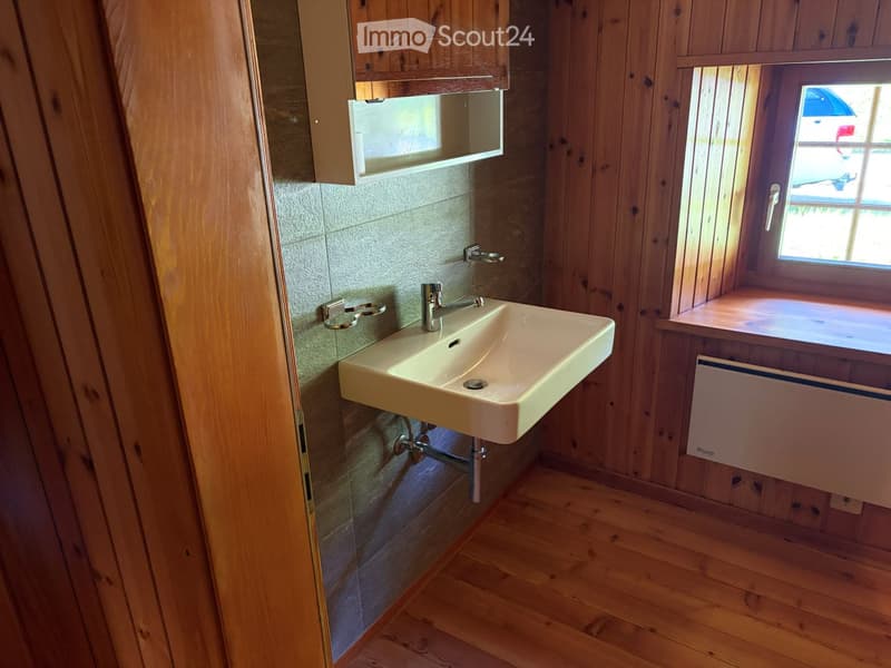Bathroom with wooden walls and floor, a white sink with a chrome faucet, a small cabinet above the sink, and a window with a wooden sill.