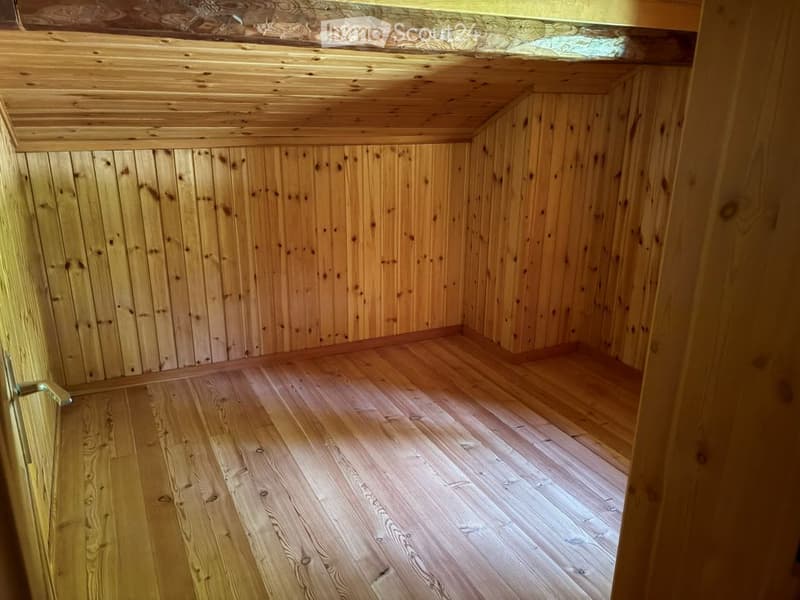 Completely empty room with wooden walls and floor, exposed wooden beams on the ceiling, and a visible door frame.