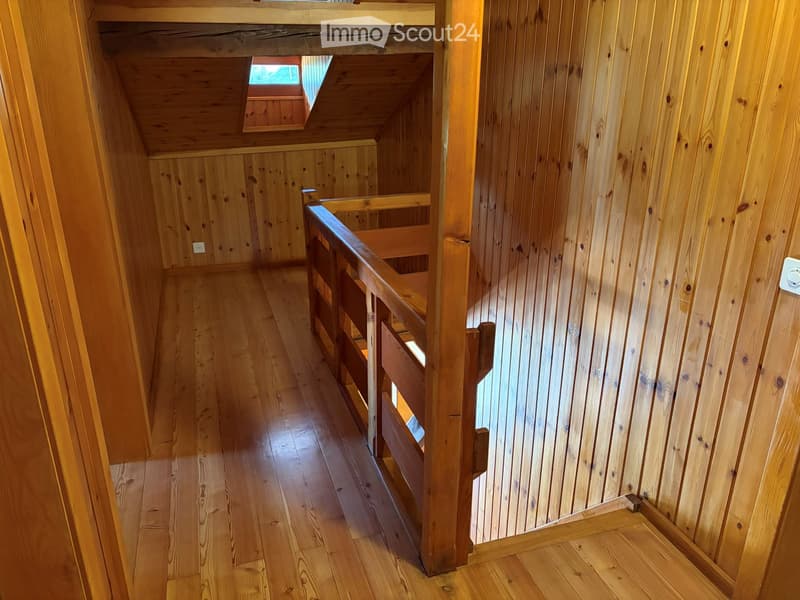Wooden staircase with a wooden railing, leading to an upper level with exposed wooden beams and a skylight window at the top.