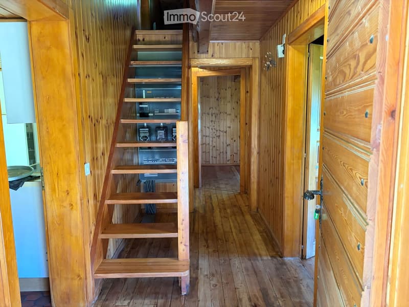 Wooden staircase leading to an upper level, wooden walls and flooring, open doorway to another room, electrical panel visible on the wall.