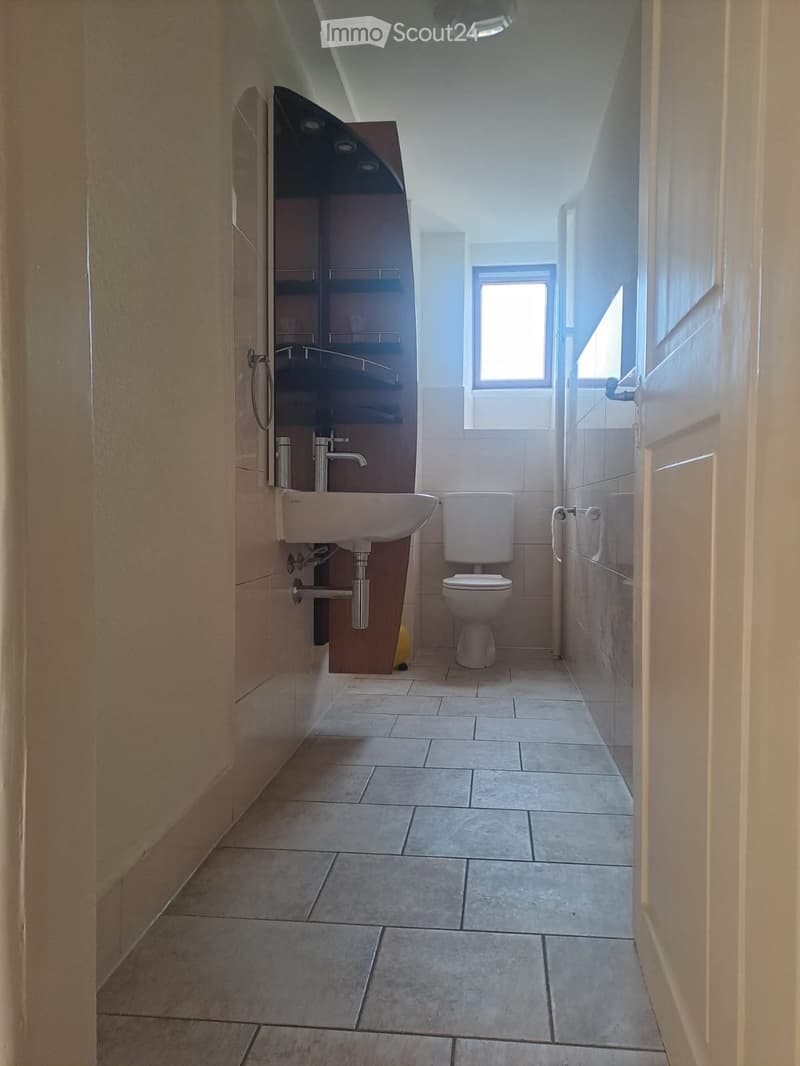 Modern bathroom with tiled floor, white sink, toilet, and built-in cabinet with shelves.