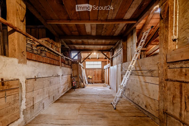 A rustic wooden hallway with exposed wooden beams and plank flooring, featuring ladders, bicycles, and storage shelves along the walls.