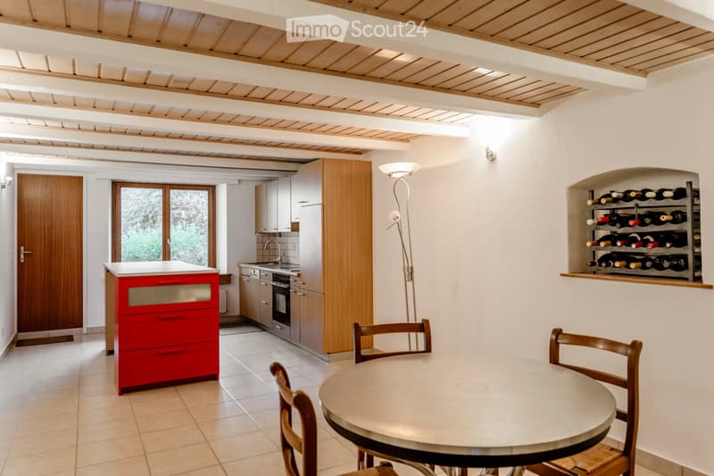 Modern kitchen with a round dining table, four chairs, a wine rack, wooden cabinets, and stainless steel appliances.