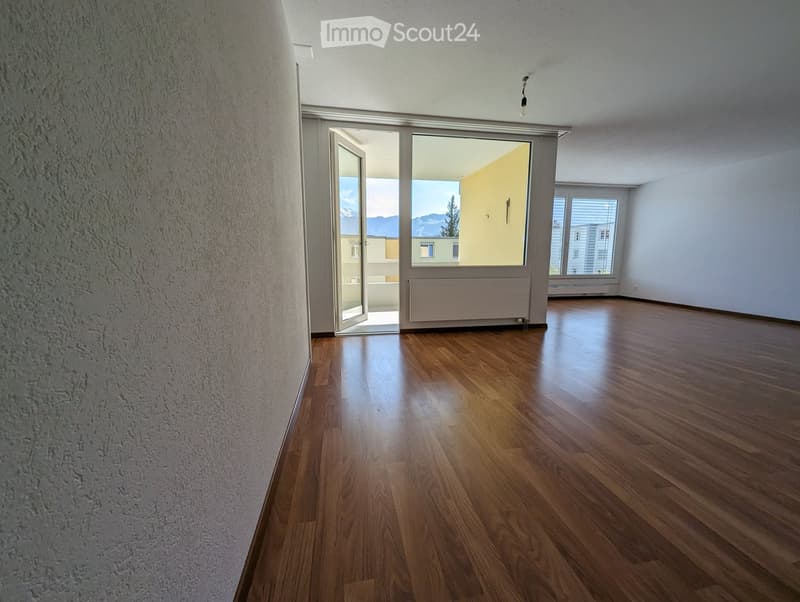 Empty room with wooden flooring, white walls, and large windows with a view of the mountains. The room features a sliding glass door leading to a balcony.