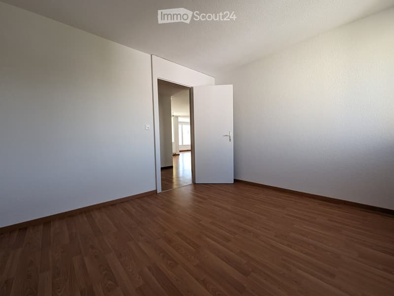 Empty room with wooden flooring and white walls, featuring a partially open white door leading to another room.