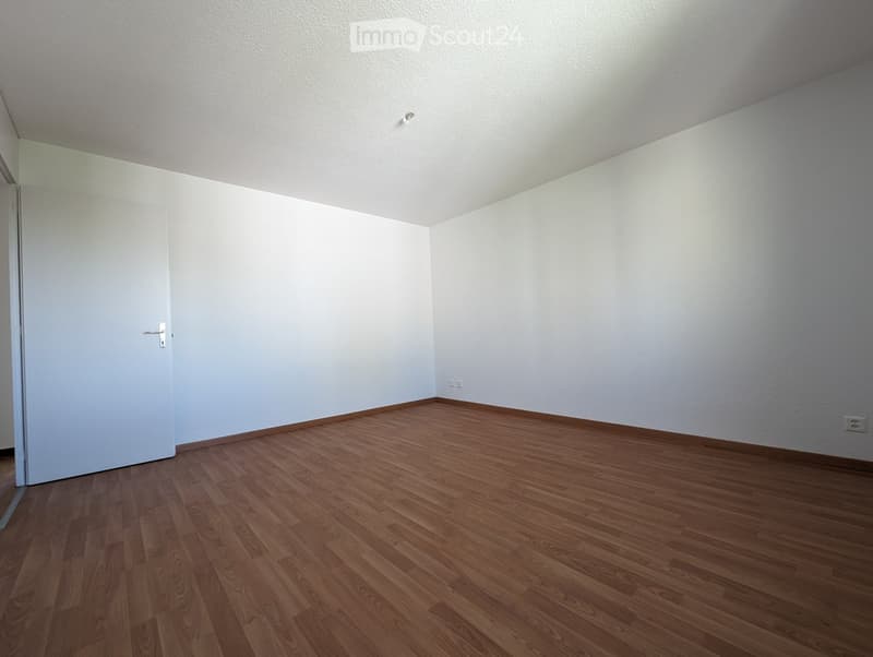 Empty room with light-colored walls and wooden flooring, featuring a single door and electrical outlets.