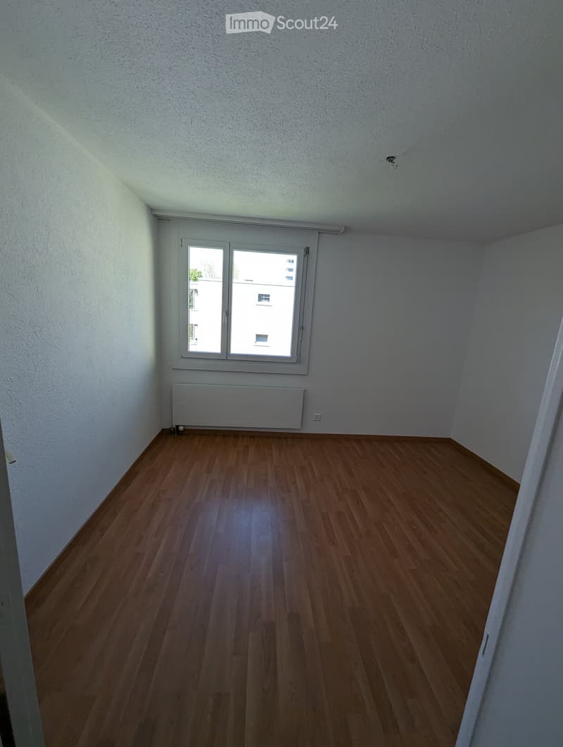 Empty room with wooden flooring, white walls, and a large window with a radiator below it.
