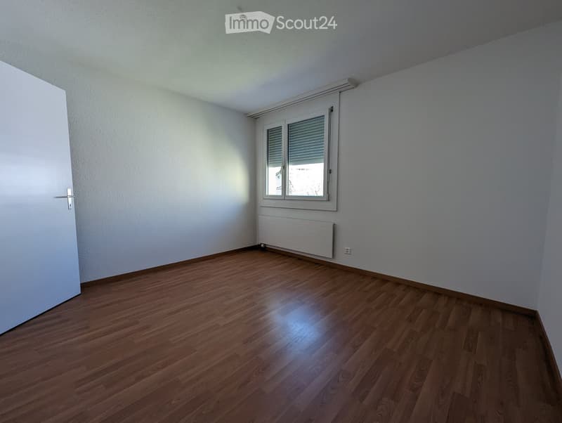 Empty room with wooden flooring, white walls, a window with blinds, and a radiator below the window.