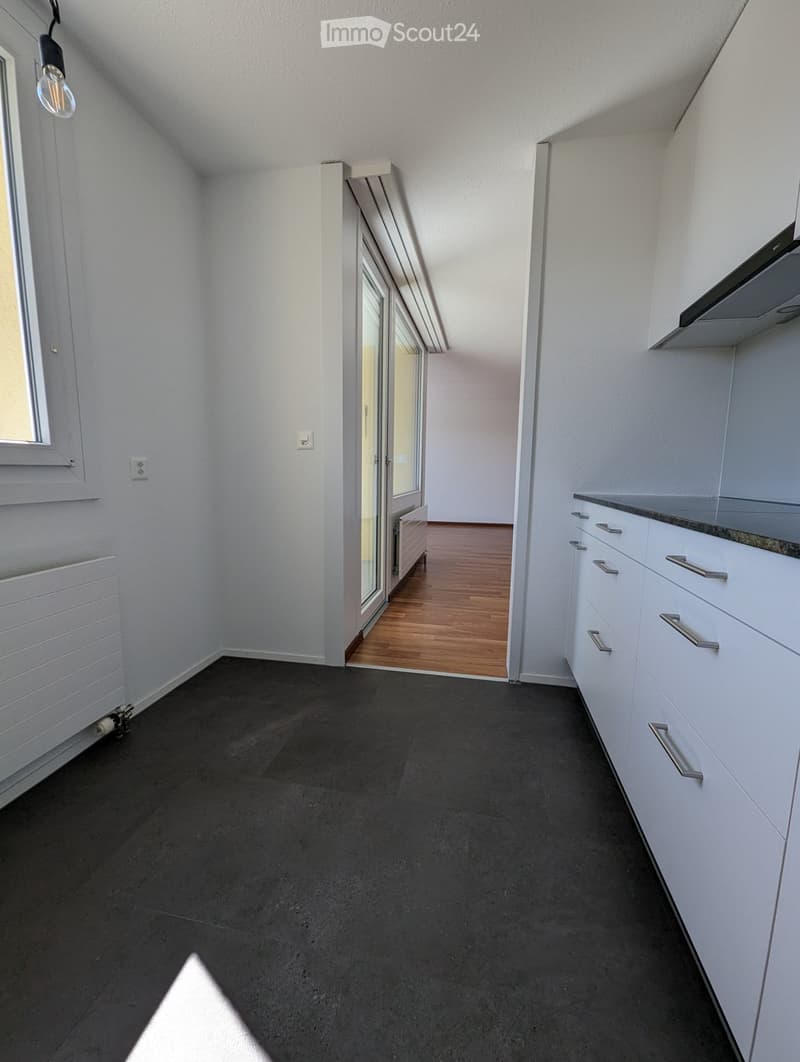 Empty room with white walls, dark grey floor, white cabinets, and a sliding glass door leading to another room with wooden flooring.