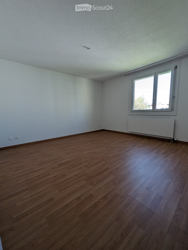 Empty room with wooden flooring, white walls, and a window with a radiator below it.